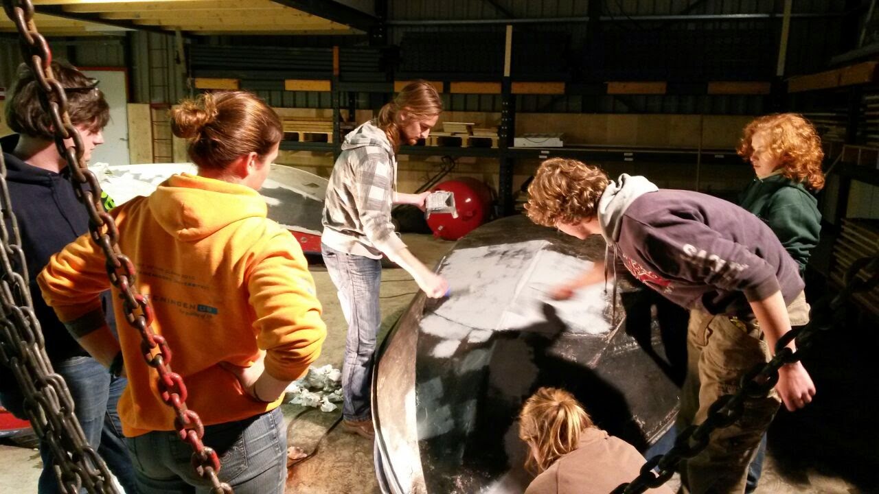 een aantal mensen staan binnen in een botenloods te werken aan een stalen boot